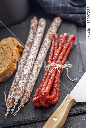 Fuet sausage with mold and smoked kabanos mini salami on black cutting board. 130972284