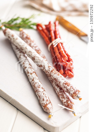 Fuet sausage with mold and smoked kabanos mini salami on white cutting board. 130972292