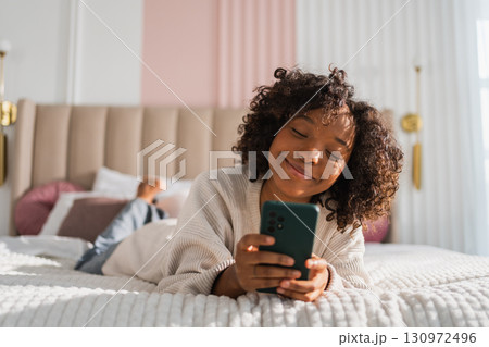 African girl holding smartphone touch screen typing scroll page at home. Woman with cell phone surfing internet using social media apps playing game. Shopping online Internet news cellphone addiction African girl holding smartphone touch screen typing scroll page at home. Woman with cell phone surfing internet using social media apps playing game. Shopping online Internet news cellphone addiction 130972496