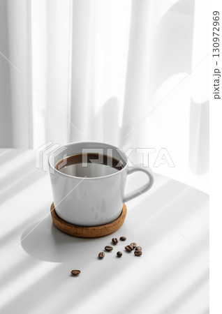 Freshly brewed espresso coffee in a cup on a white table near window with coffee beans 130972969