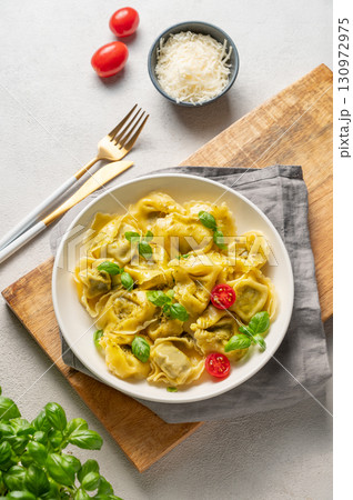 Tortellini pasta with parmesan, pesto and basil in a plate on a wooden board on a light  background 130972975