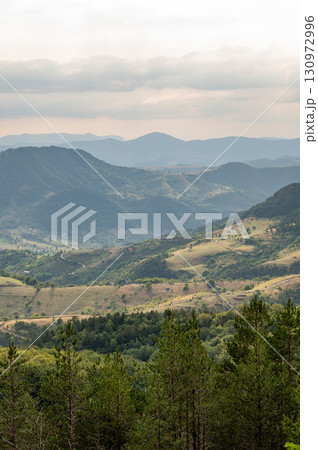 Panoramic view of green forested mountains and valleys under gloomy cloudy sky Panoramic view of green forested mountains and valleys under gloomy cloudy sky 130972996