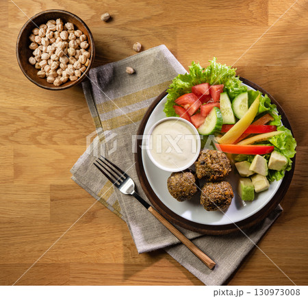 Falafel balls with lettuce, tomatoes, cucumbers, peppers, avocado and sauce on a plate  130973008
