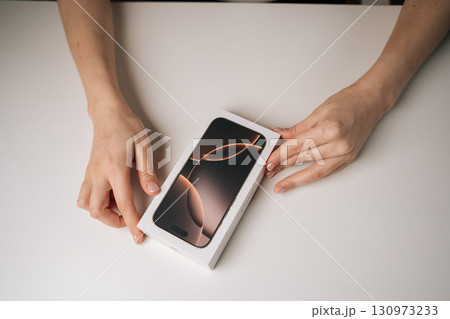 Ufa, Russia - 17 August 2025. Top view of unrecognizable woman opening pristine white box of brand new iPhone 16 pro, revealing sleek device within, moment of anticipation and technological discovery. Ufa, Russia - 17 August 2025. Top view of unrecognizable woman opening pristine white box of brand new iPhone 16 pro, revealing sleek device within, moment of anticipation and technological discovery. 130973233