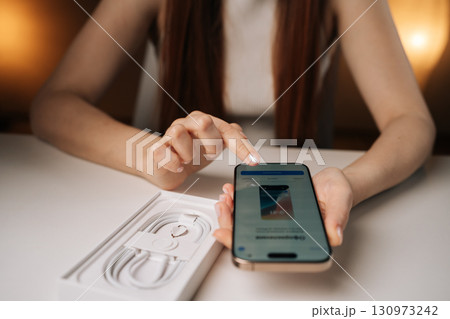 Ufa, Russia - 17 August 2025. Woman unpacking new iPhone 16 pro, examining sleek device and innovative features while setting up smartphone for very first time, unpacking process of latest smartphone 130973242