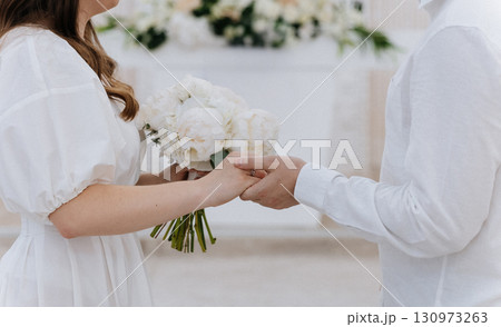 Bride and groom holding hands with a bouquet during intimate wedding ceremony Bride and groom holding hands with a bouquet during intimate wedding ceremony 130973263