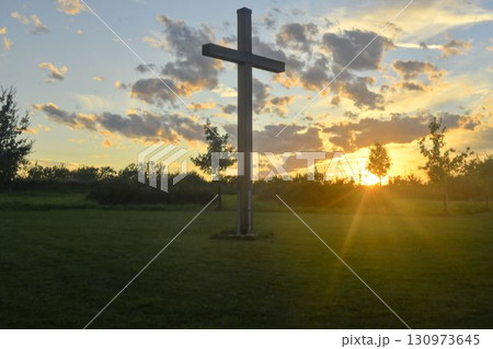 A large Christian cross in the scenery of a landscape. A Christian cross lighted by the setting sun. The concept of religion and Christianity. A large Christian cross in the scenery of a landscape. A Christian cross lighted by the setting sun. The concept of religion and Christianity. 130973645