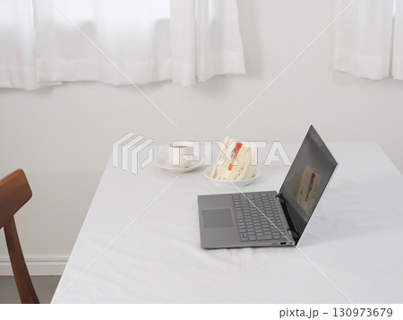 白いテーブルの上のノートパソコンとカフェオレとサンドイッチ 130973679