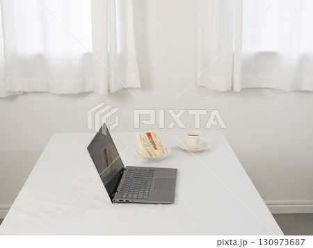 白いテーブルの上のノートパソコンとカフェオレとサンドイッチ 130973687