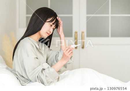 ベッドで体温を測る体調不良の若いアジア人女性(発熱,風邪) ベッドで体温を測る体調不良の若いアジア人女性(発熱,風邪) 130976554