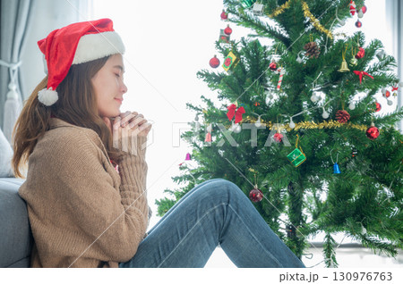 Catholic woman praying to god after decorated a Christmas tree during Christmas festival. By raising hands in prayer, the worshipper approaches the realm of the heavenly gods. 130976763