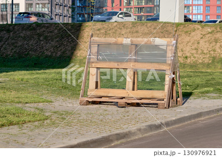 A wooden frame, covered in transparent plastic, stands amidst a vibrant urban landscape 130976921