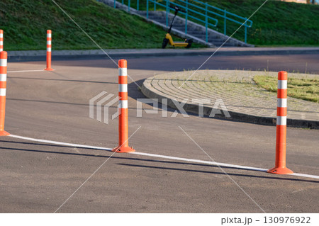 Bright orange traffic cones line the edge of a pathway, guiding pedestrians safely along a well-maintained route beside a grassy area under clear blue skies Bright orange traffic cones line the edge of a pathway, guiding pedestrians safely along a well-maintained route beside a grassy area under clear blue skies 130976922