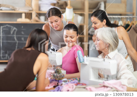 Young female teacher shows group how to sew Young female teacher shows group how to sew 130978013