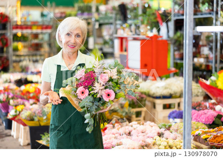 Mature female florist preparing bouquet with roses and gerberas in floral shop Mature female florist preparing bouquet with roses and gerberas in floral shop 130978070