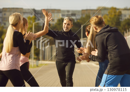 Happy people giving high five to mature man rejoicing the success in sport training outdoors. Happy people giving high five to mature man rejoicing the success in sport training outdoors. 130978115