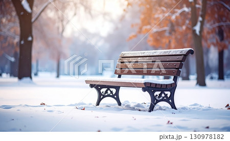 A wooden bench in a serene winter park is covered with a soft layer of white snow A wooden bench in a serene winter park is covered with a soft layer of white snow 130978182
