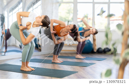Young woman with group of active people exercising full body stretching workout during yoga classes in gym Young woman with group of active people exercising full body stretching workout during yoga classes in gym 130978321