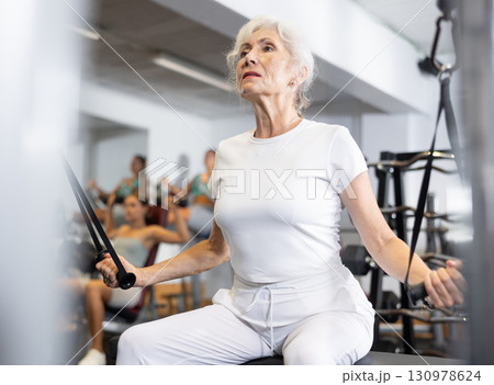 Mature woman working on special machine with ropes to develop arm muscles 130978624