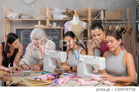 Sewing teacher helping female student with machine threading in workshop Sewing teacher helping female student with machine threading in workshop 130978738