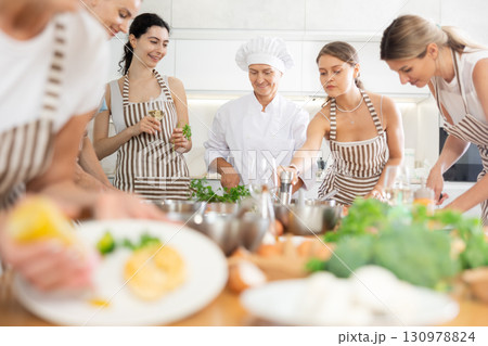 Mature female cook teaching members of cooking course over glass of wine 130978824