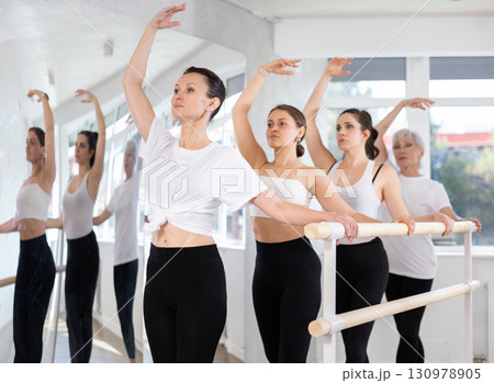 Woman maintaining third position at ballet barre at group rehearsal Woman maintaining third position at ballet barre at group rehearsal 130978905