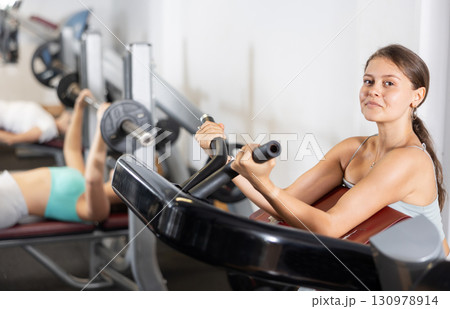 Sporty girl pumps up her arm muscles on a special exercise machine in gym 130978914