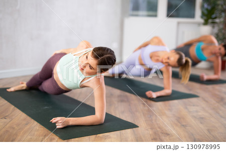 Diligent women practicing plank pose of yoga in light fitness room 130978995