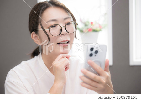 スマホを見て眼鏡で考える笑顔の40代女性のクローズアップ 130979155