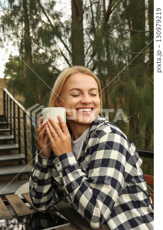 Smiling woman enjoys a warm drink outdoors Smiling woman enjoys a warm drink outdoors 130979219