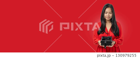 A woman in a red dress admires a black gift box A woman in a red dress admires a black gift box 130979255