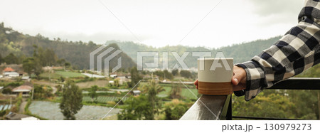 Holding a warm cup of coffee while enjoying scenic views Holding a warm cup of coffee while enjoying scenic views 130979273