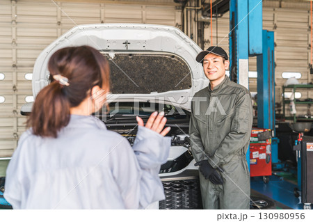 整備工場で車の説明をする整備士の男性スタッフとドライバーの女性客 整備工場で車の説明をする整備士の男性スタッフとドライバーの女性客 130980956