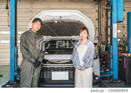 整備工場でリフトアップされた車の前にいる整備士の男性スタッフと女性客 整備工場でリフトアップされた車の前にいる整備士の男性スタッフと女性客 130980959