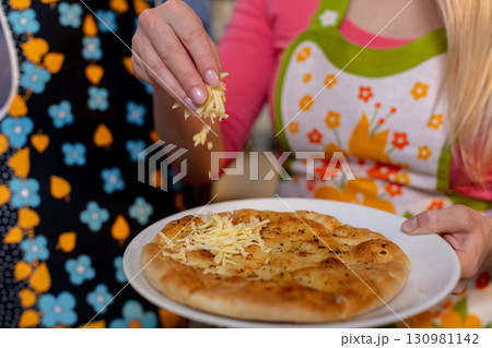 Indulge in the incredibly delicious preparation of homemade pizza with a cheesy topping 130981142