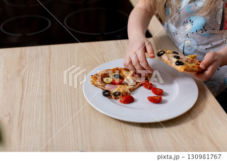 A Happy Child Is Delightfully Enjoying Tasty Pizza with Fresh Ingredients in a Bright Kitchen 130981767