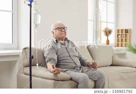 Senior man sitting on couch at home while receiving IV drip infusion and vitamin therapy Senior man sitting on couch at home while receiving IV drip infusion and vitamin therapy 130981792