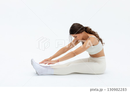 A Young Woman Engaging in Stretching Exercises Within a Minimalist Studio Environment 130982283