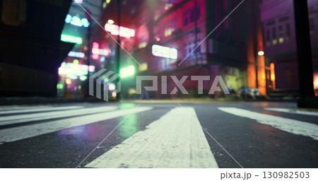 A vibrant street view features neon lights illuminating a wet urban landscape at night. The ground shows striped crosswalks, while colorful lights create a lively atmosphere. 130982503