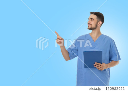 Doctor in scrubs is holding a clipboard and gesturing upwards 130982921