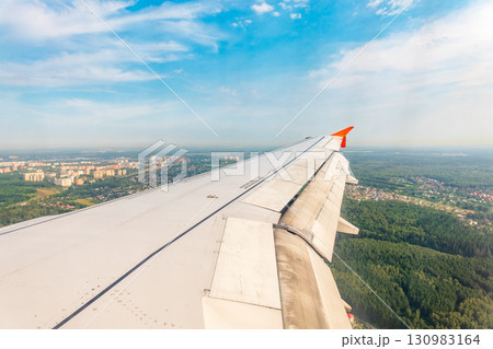 View of airplane wing, blue skies and green land during landing. Airplane window view. 130983164