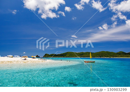 嘉比島の白砂のビーチには観光客が上陸している。 パラソルやボート、サバニが停まっている美しいサンゴ礁 130983299