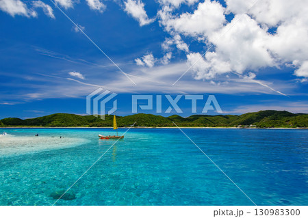 嘉比島の白砂のビーチには観光客が上陸している。 パラソルやボート、サバニが停まっている美しいサンゴ礁 130983300