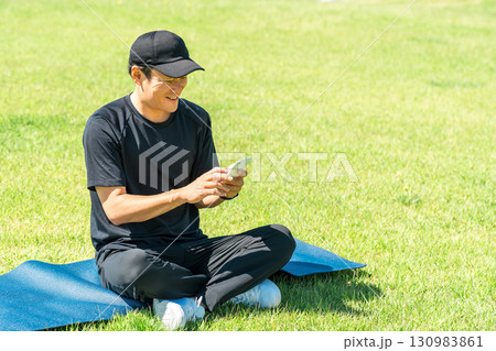 公園の芝生に座りスマホを使うスポーツウェア姿のアジア人男性 公園の芝生に座りスマホを使うスポーツウェア姿のアジア人男性 130983861