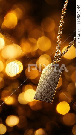 Close-up of a silver pendant on a delicate chain, suspended against a warm golden bokeh background, creating a dreamy atmosphere. 130984244