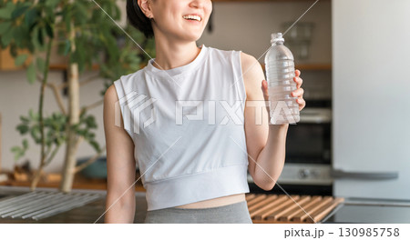 自宅トレーニング後にペットボトルのミネラルウォーターで水分補給をするアジア人女性 自宅トレーニング後にペットボトルのミネラルウォーターで水分補給をするアジア人女性 130985758