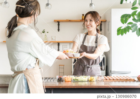 キッチン,カウンターから食事を手渡すエプロン姿のカフェ店員のアジア人女性 130986070