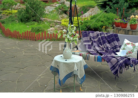 Apple blossoms on a table in front of a sofa swing in the courtyard of a country house. Apple blossoms on a table in front of a sofa swing in the courtyard of a country house. 130986255