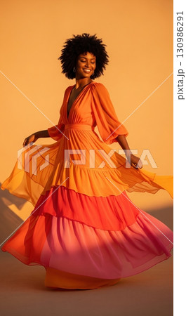 Happy black woman with an afro hairstyle dancing in a long flowing colorful tiered dress Happy black woman with an afro hairstyle dancing in a long flowing colorful tiered dress 130986291