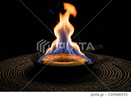 Flambeed banana dessert with spectacular blue and orange flames in a cast iron skillet 130986435